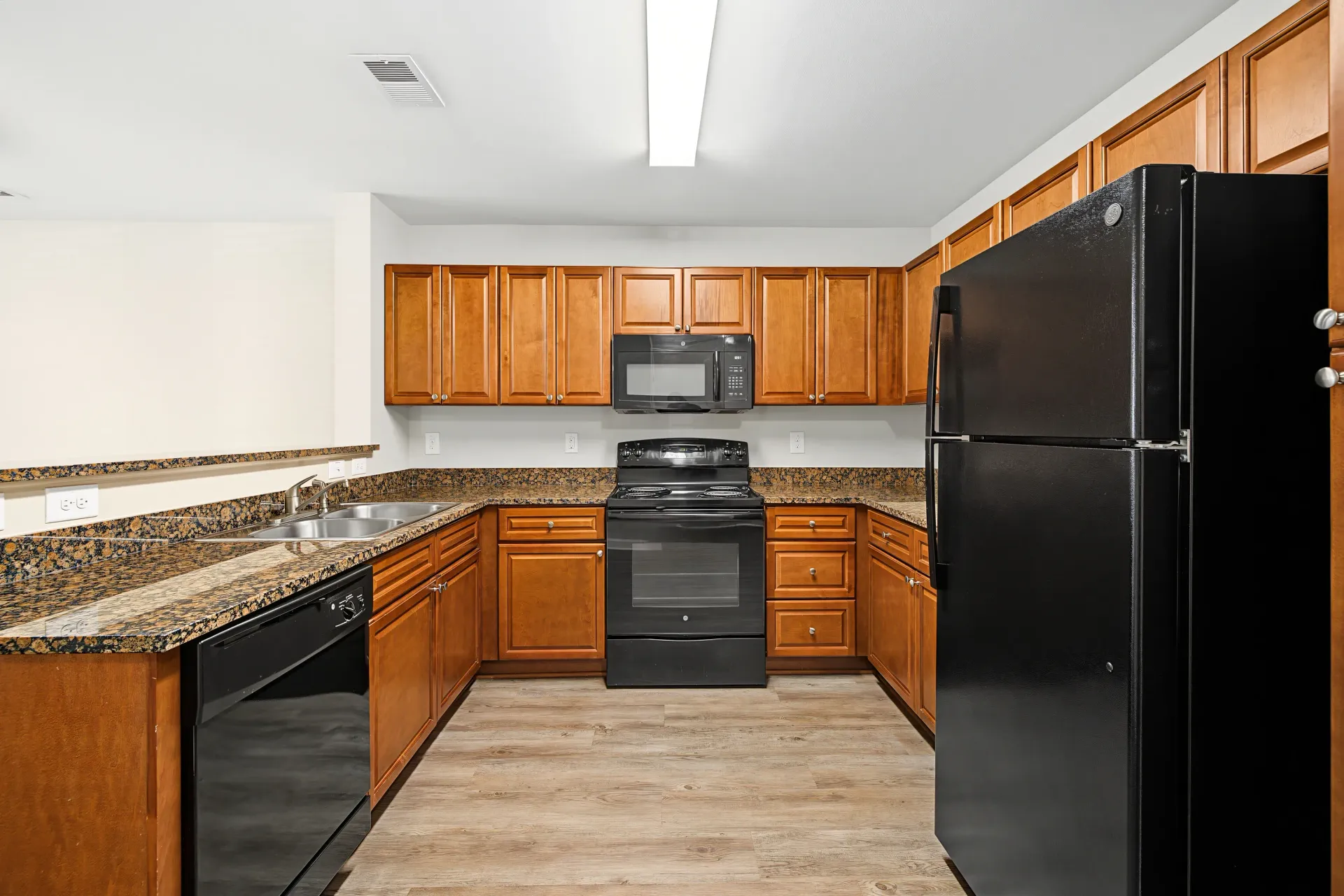 Kitchen with wood cabinets, black appliances, and granite countertops.