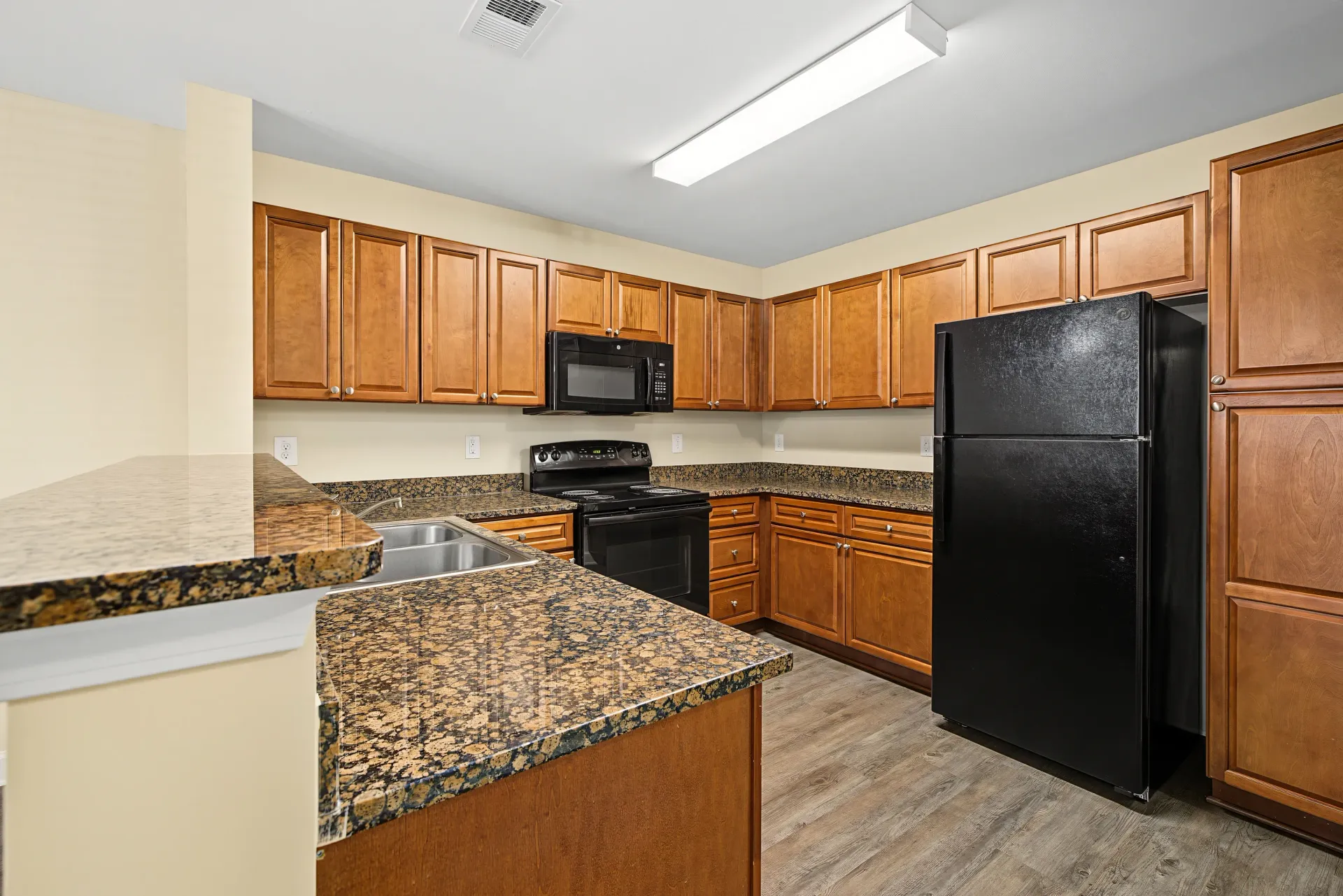 Kitchen with granite countertops, wooden cabinets, black appliances including a refrigerator, stove, and microwave.