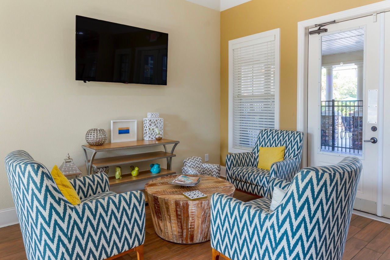 Apartment living room with blue chevron chairs, a round wood coffee table, and a wall-mounted TV at Stone Gables.