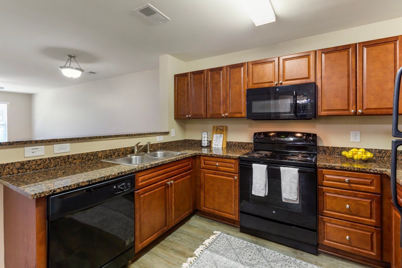 Kitchen with brown wood cabinets, granite countertops, double sink, and black appliances at Stone Gables.