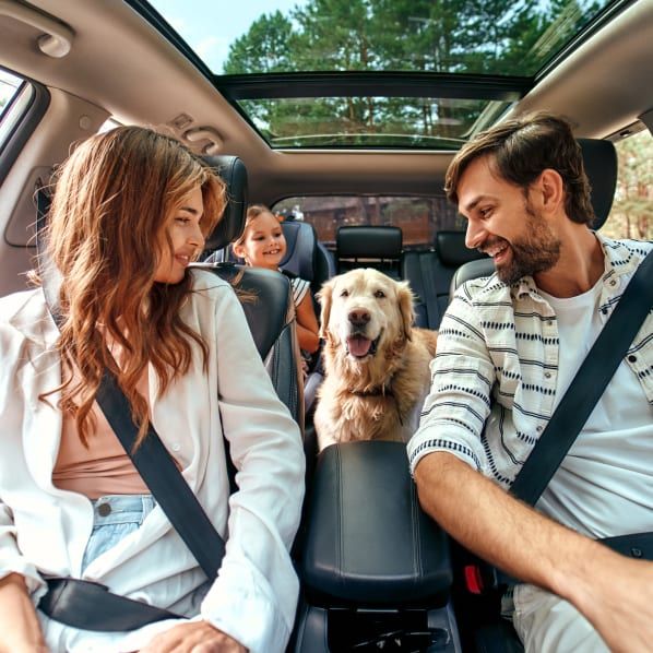 A family and their golden retriever inside a car with a panoramic sunroof, smiling at each other during a drive.