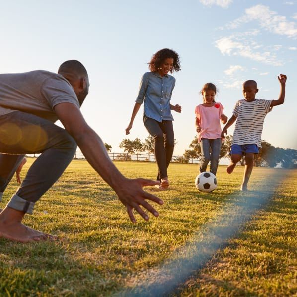 A family plays soccer together in a grassy field during a sunny day.