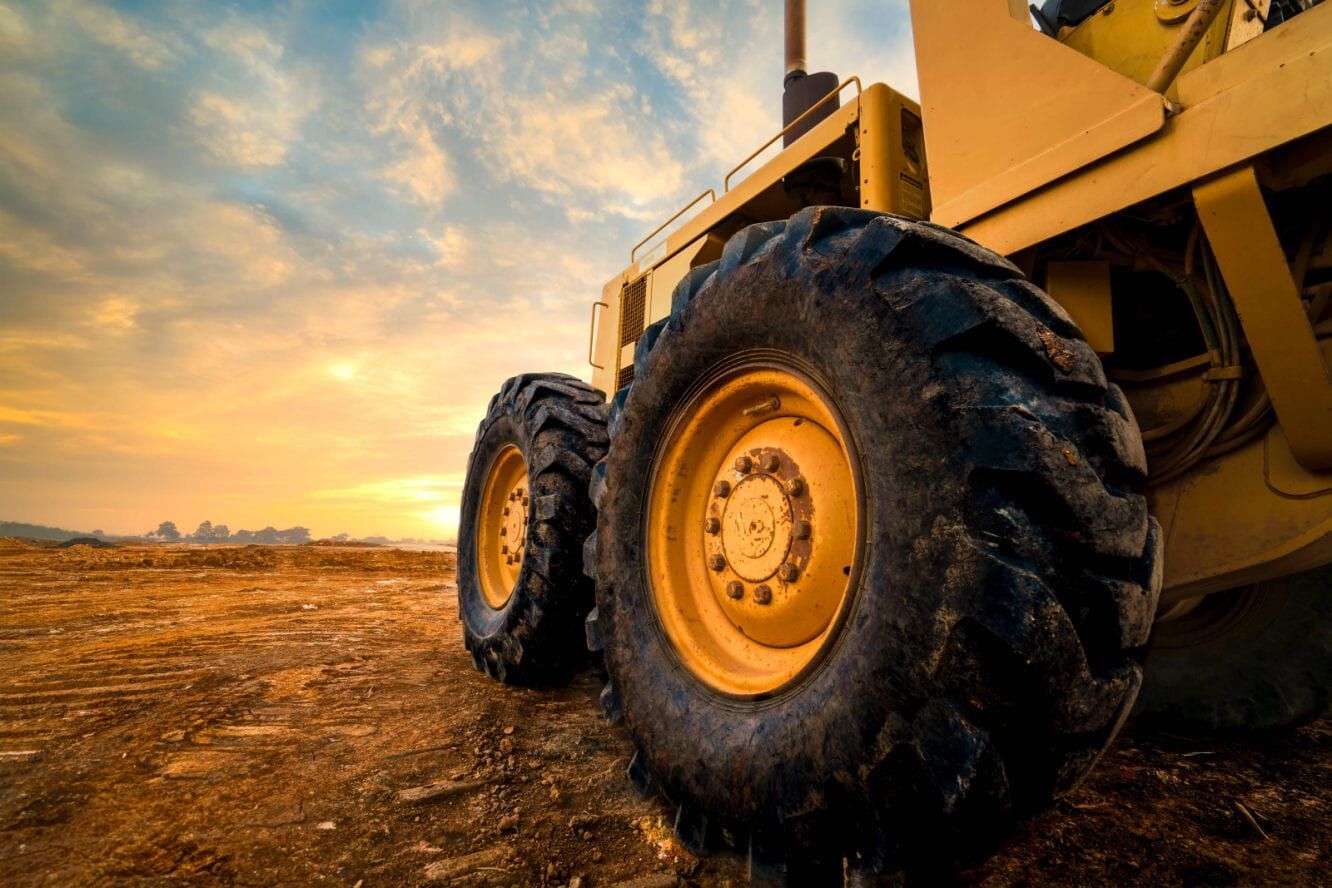 Yellow Construction Grader on a Dirt Field With a Sunrise Sky Behind It — Wheel Alignment Centre in Braitling, NT