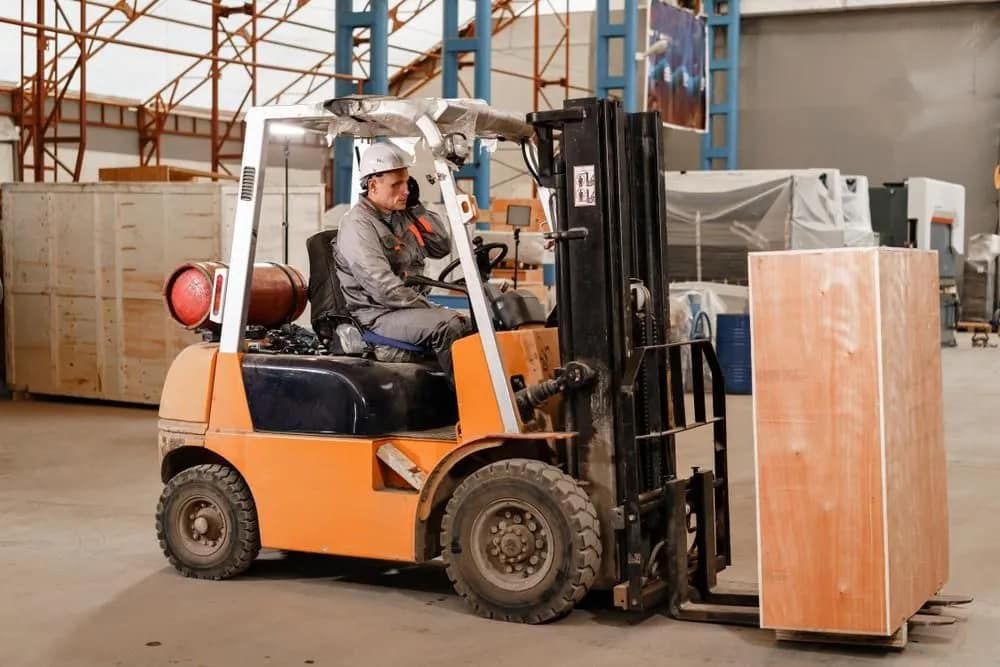 Forklift Operator in Orange Forklift, Moving Wooden Crate in Warehouse — Wheel Alignment Centre in Braitling, NT
