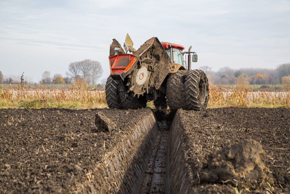 Red Tractor With a Trenching Attachment Digging a Ditch in a Muddy Field — Wheel Alignment Centre in Braitling, NT
