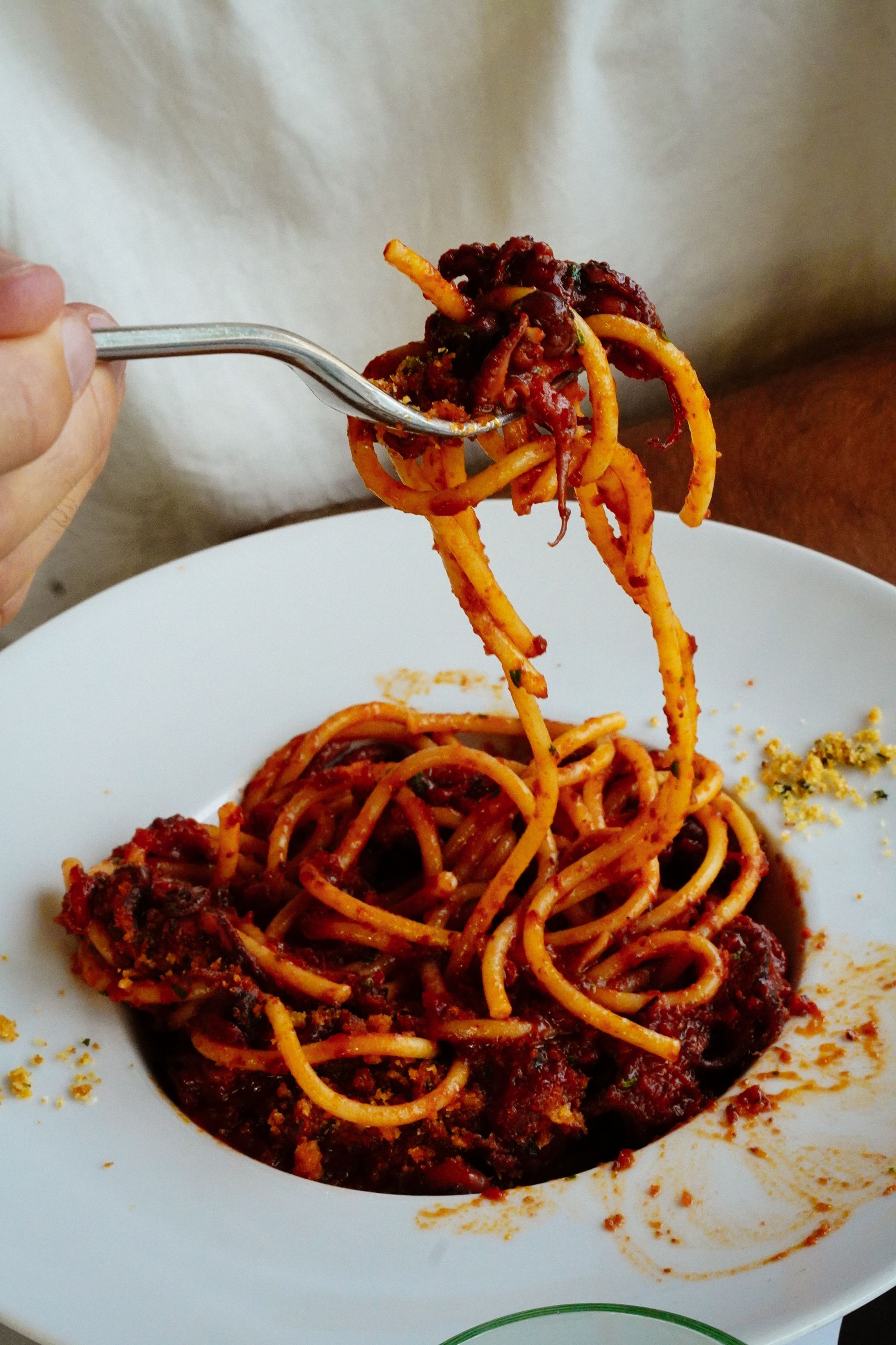 Donna sorridente che tiene in mano una forchetta con la pasta sopra un piatto di pasta. Sfondo sfocato.