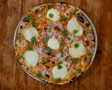 Pizza con mozzarella, pesto e formaggio grattugiato su un piatto bianco, appoggiata su un tavolo di legno.