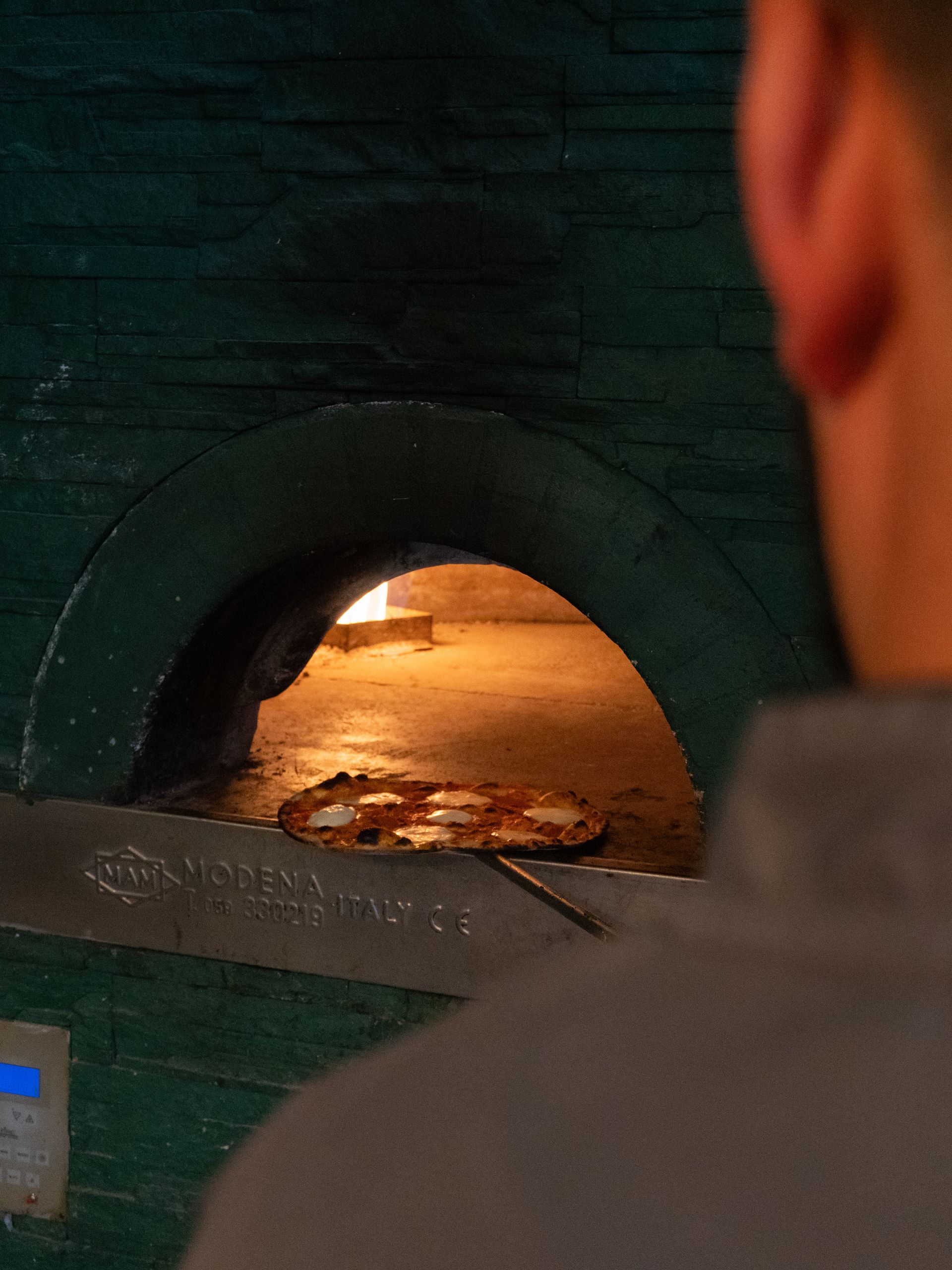 Persona che guarda dentro un forno per pizza; pizza sulla pala all'interno.