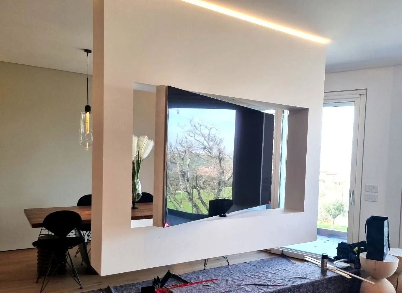 Una grande parete dai colori chiari con TV integrata. Sono visibili una zona pranzo e una vista esterna.