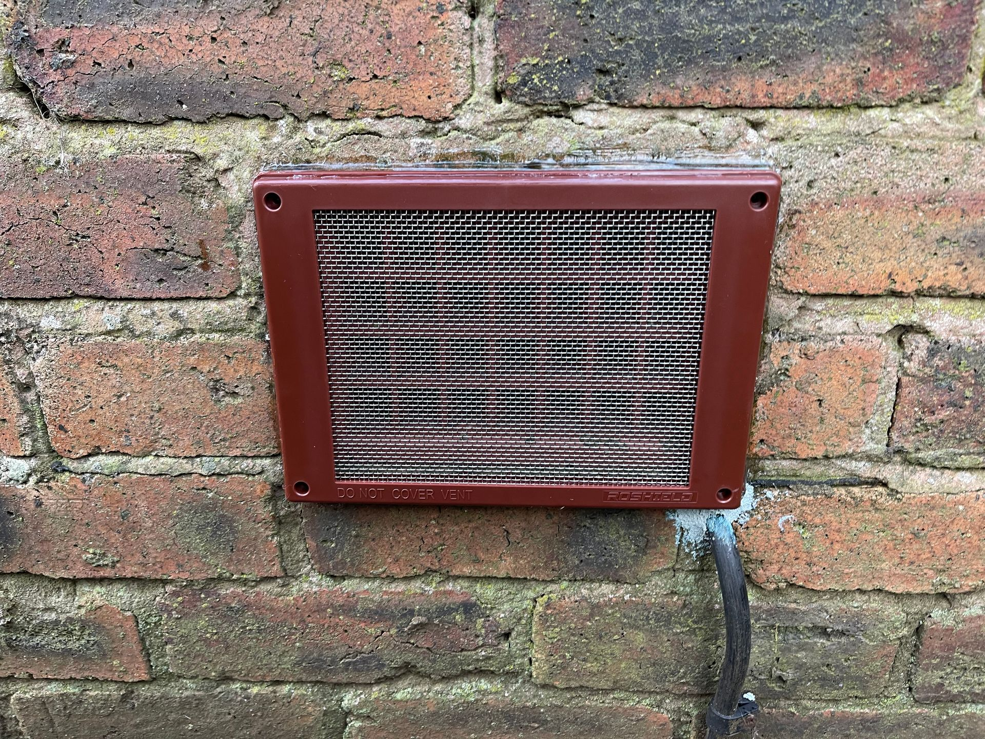 Gray wall vent grate set into a beige exterior wall near the ground