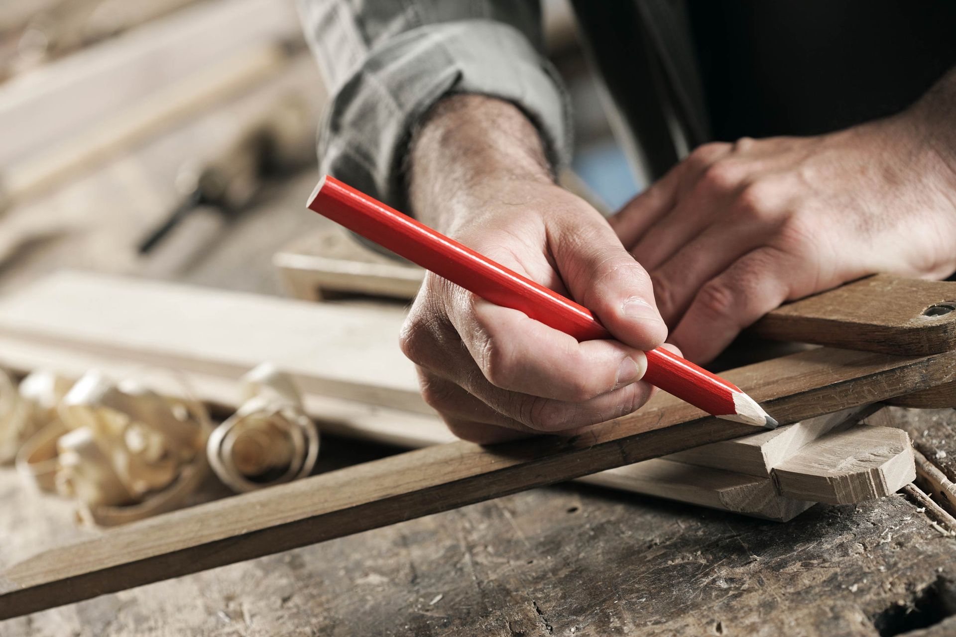 A man is measuring a piece of wood with a red pencil