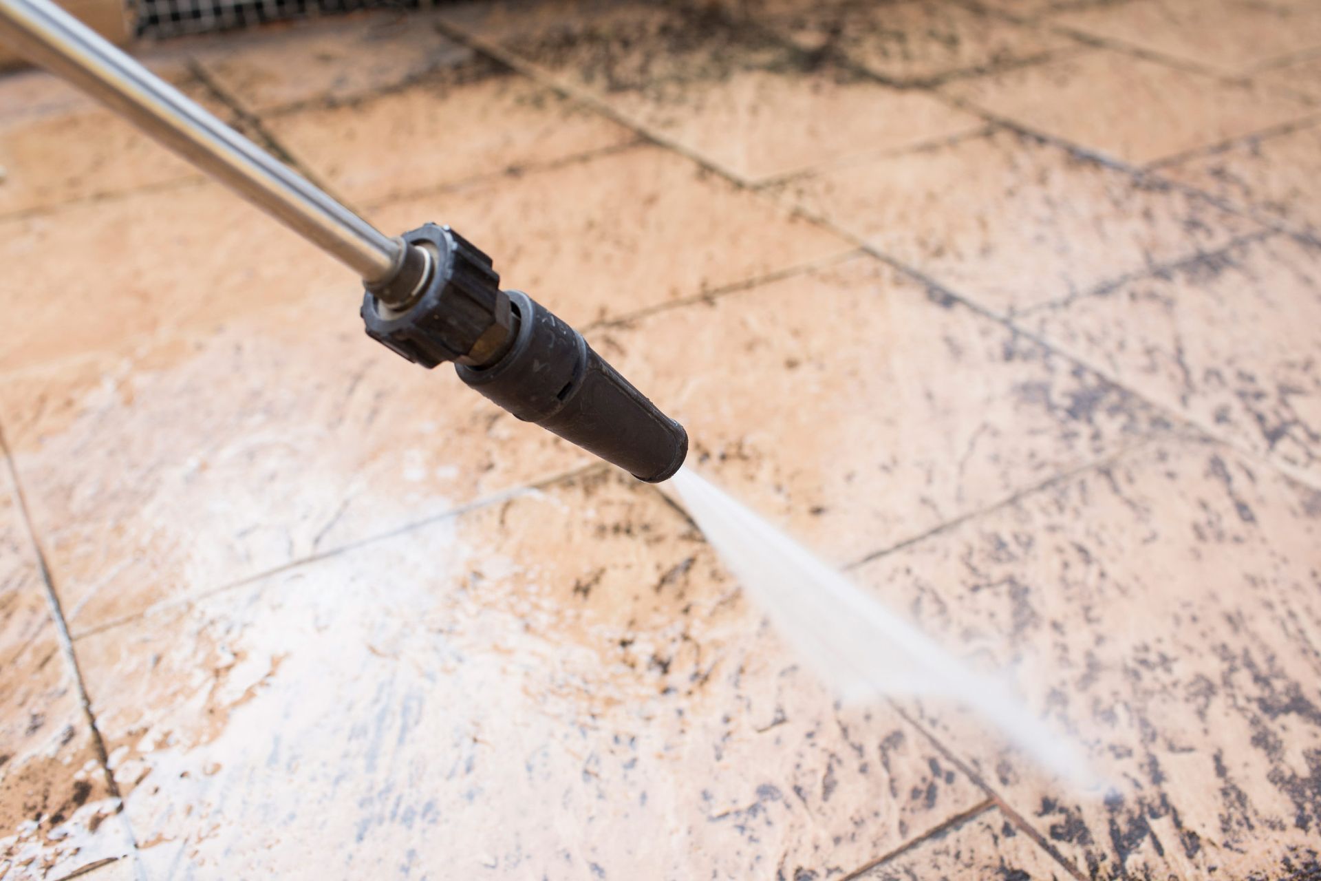 A person is using a high pressure washer to clean a tile floor.
