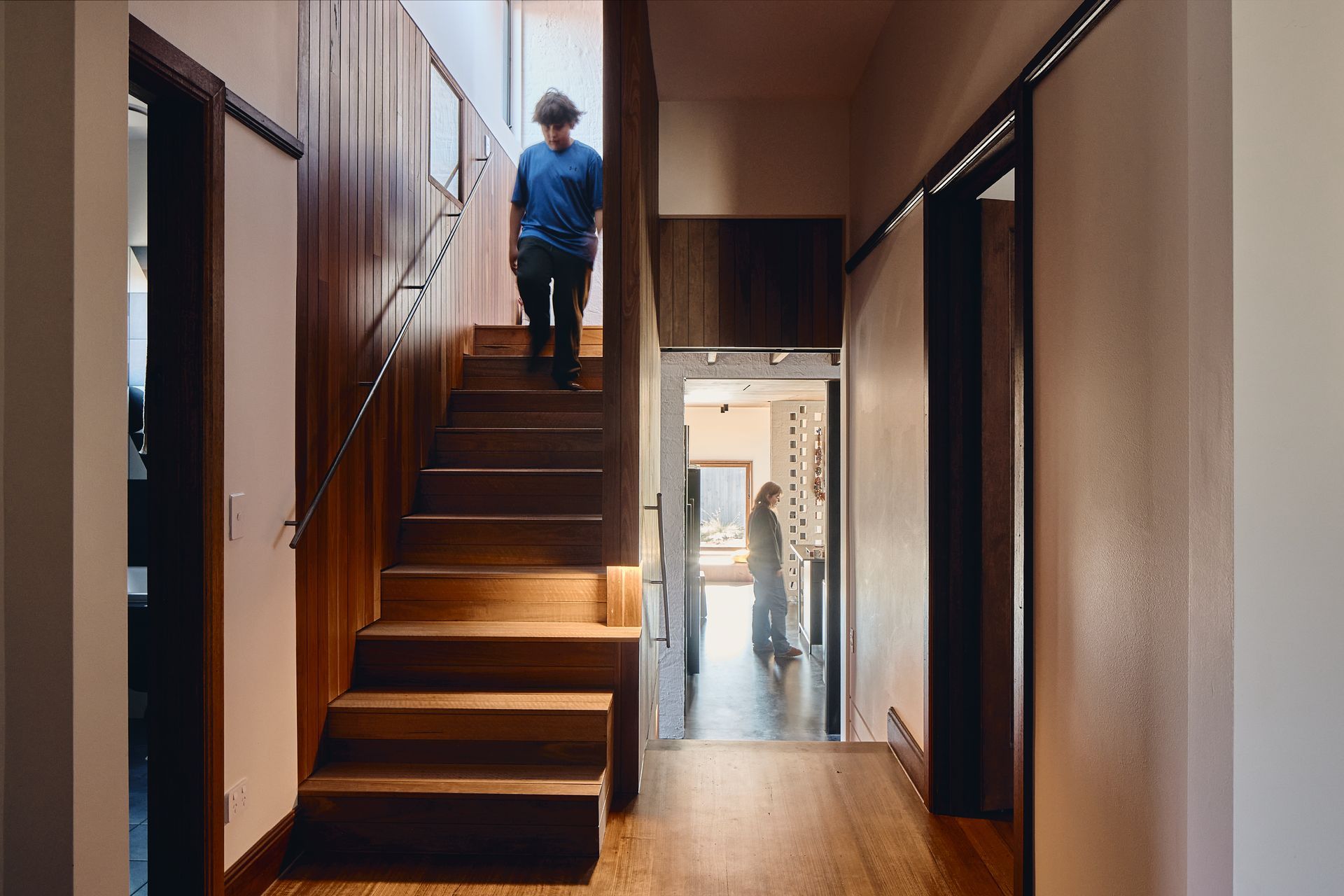 A man is walking up a set of wooden stairs in a hallway.