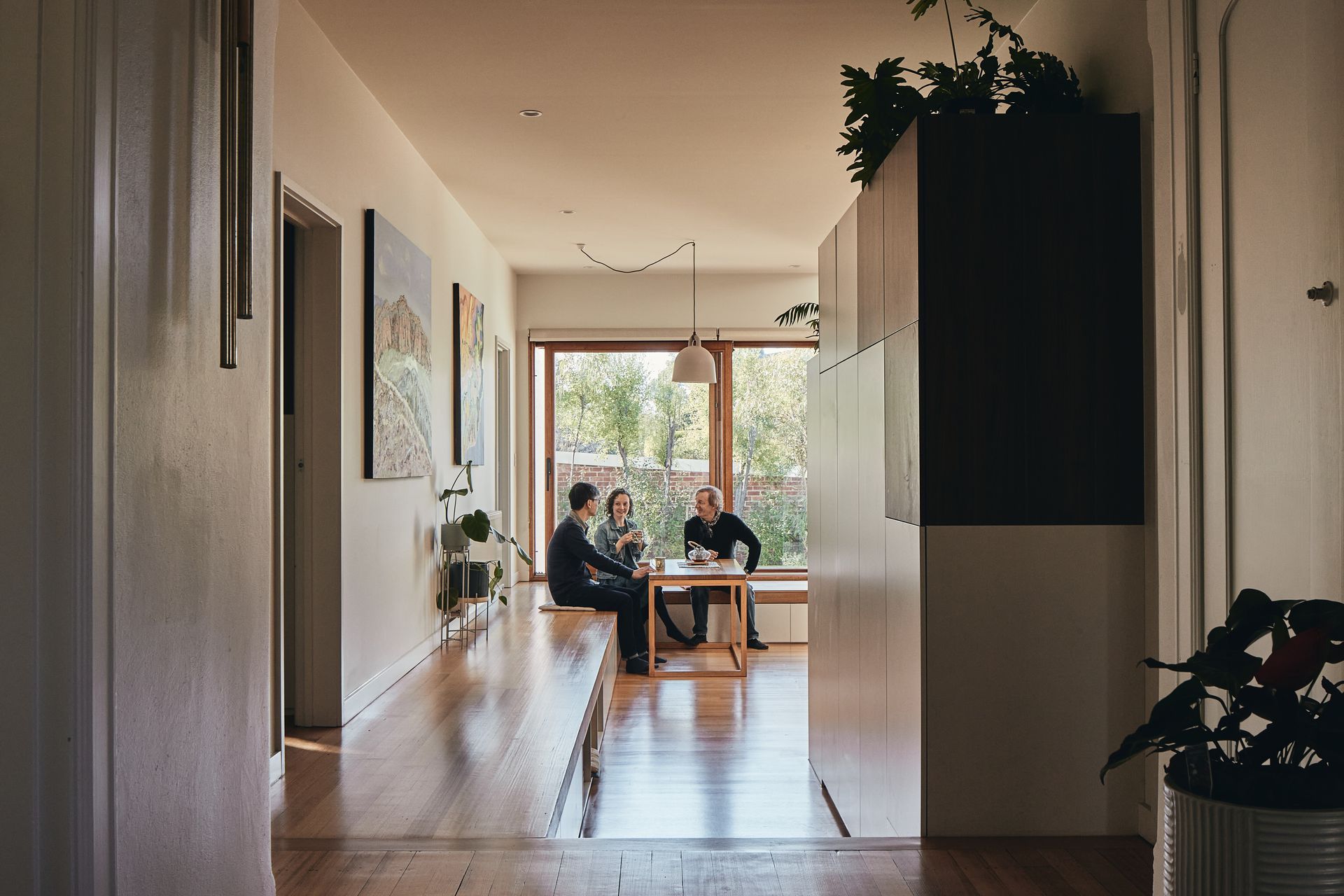 Three people are sitting at a timber dining table in a living room.