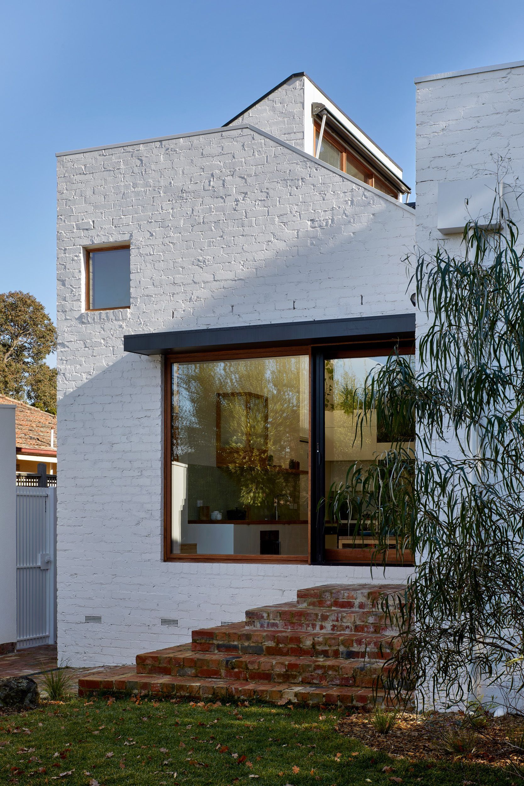 A white brick house with a large window and stairs leading up to it.