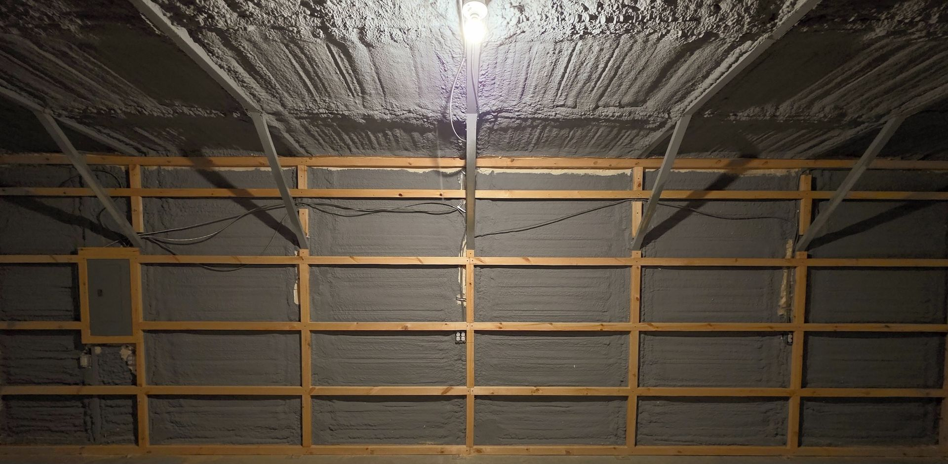 Empty industrial ceiling with spray-foam insulation and metal framing above a wall grid
