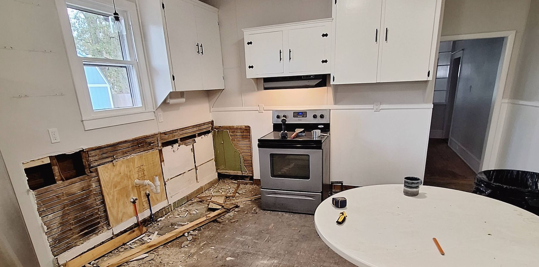 Damaged kitchen with missing cabinets, exposed wall, stove, and debris on the floor