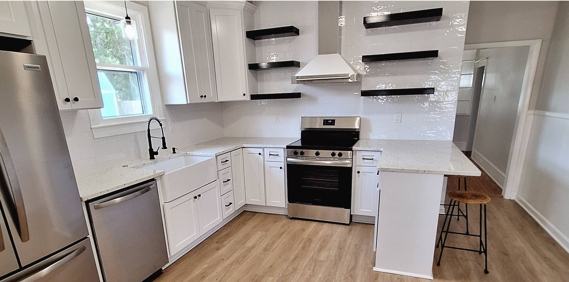 Modern white kitchen with stainless steel appliances, black countertops, and wood flooring
