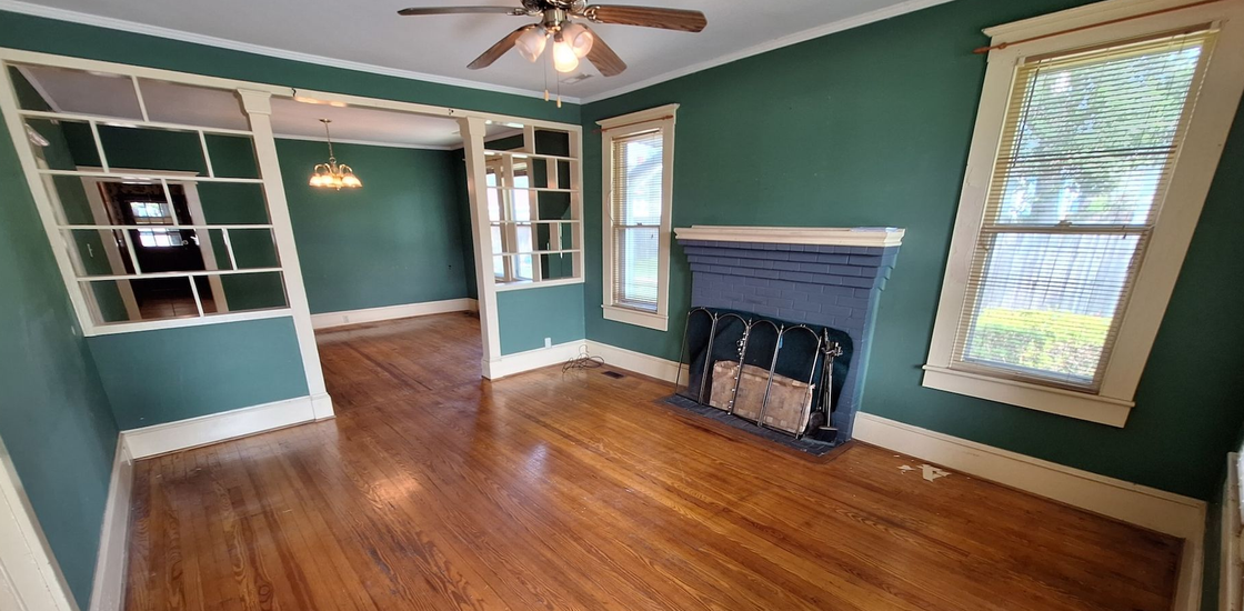 Empty teal living room with hardwood floors, fireplace, ceiling fan, and built-in shelves