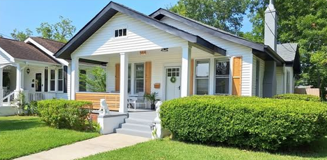 Single-story white house with porch, gray roof, and green lawn on a sunny day