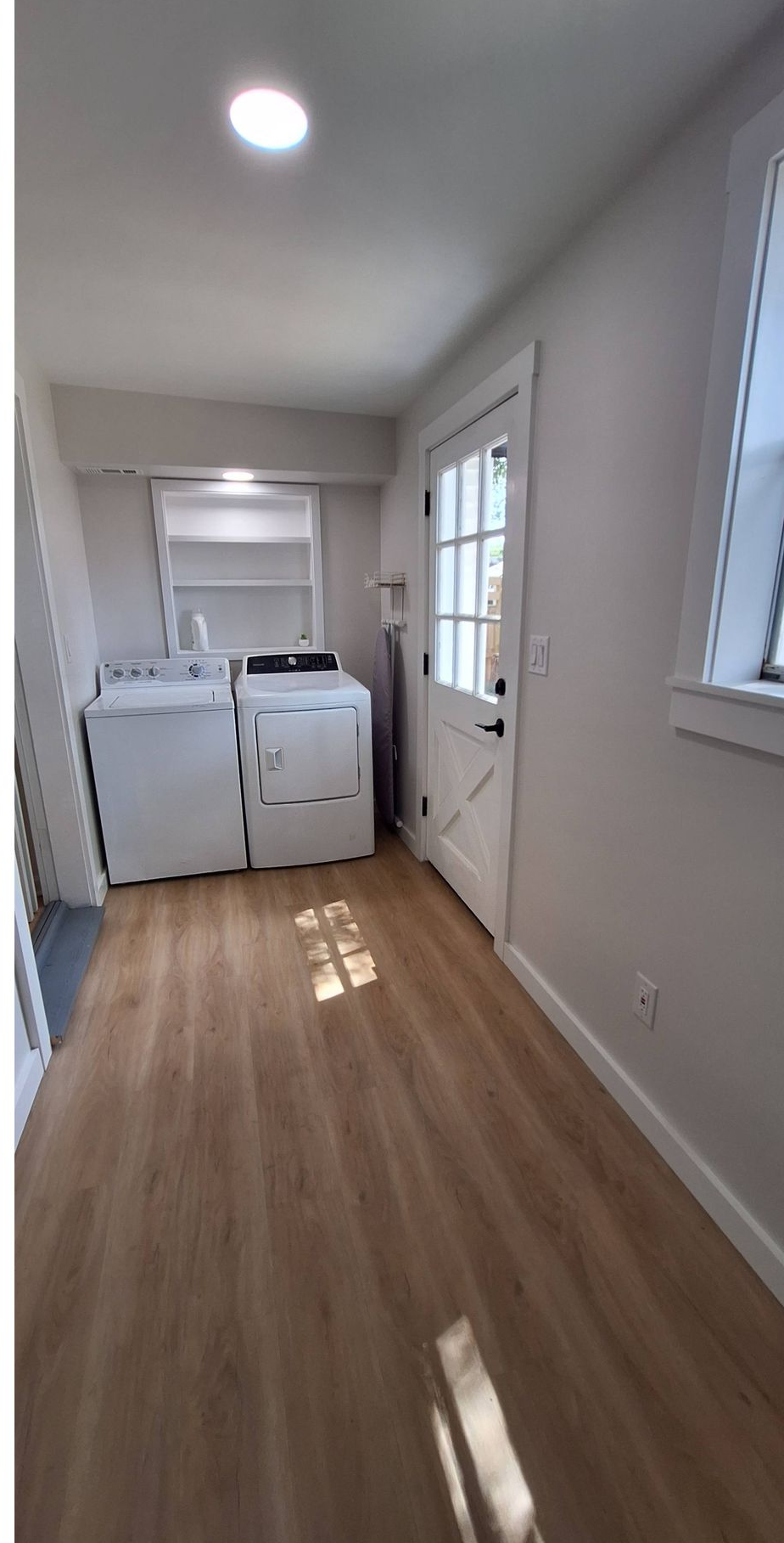 Narrow laundry room with washer and dryer, white walls, wood floor, and bright daylight from windows