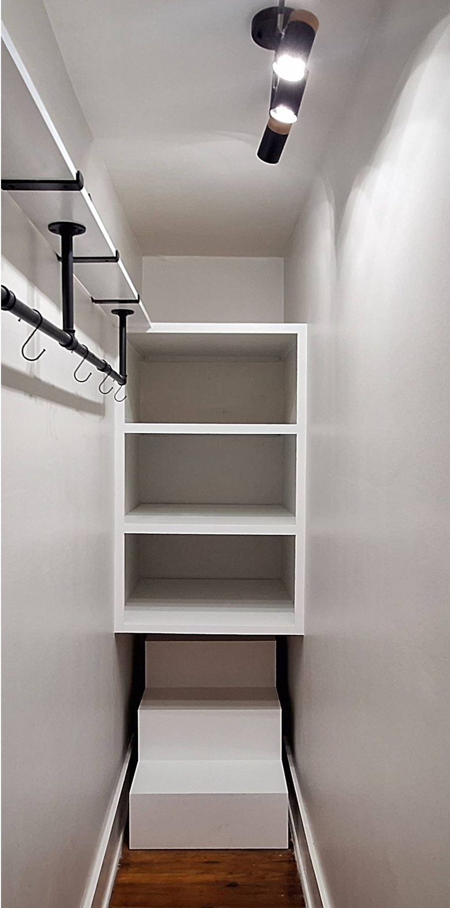Small white walk-in closet with shelves, hanging rod, and ceiling track light.