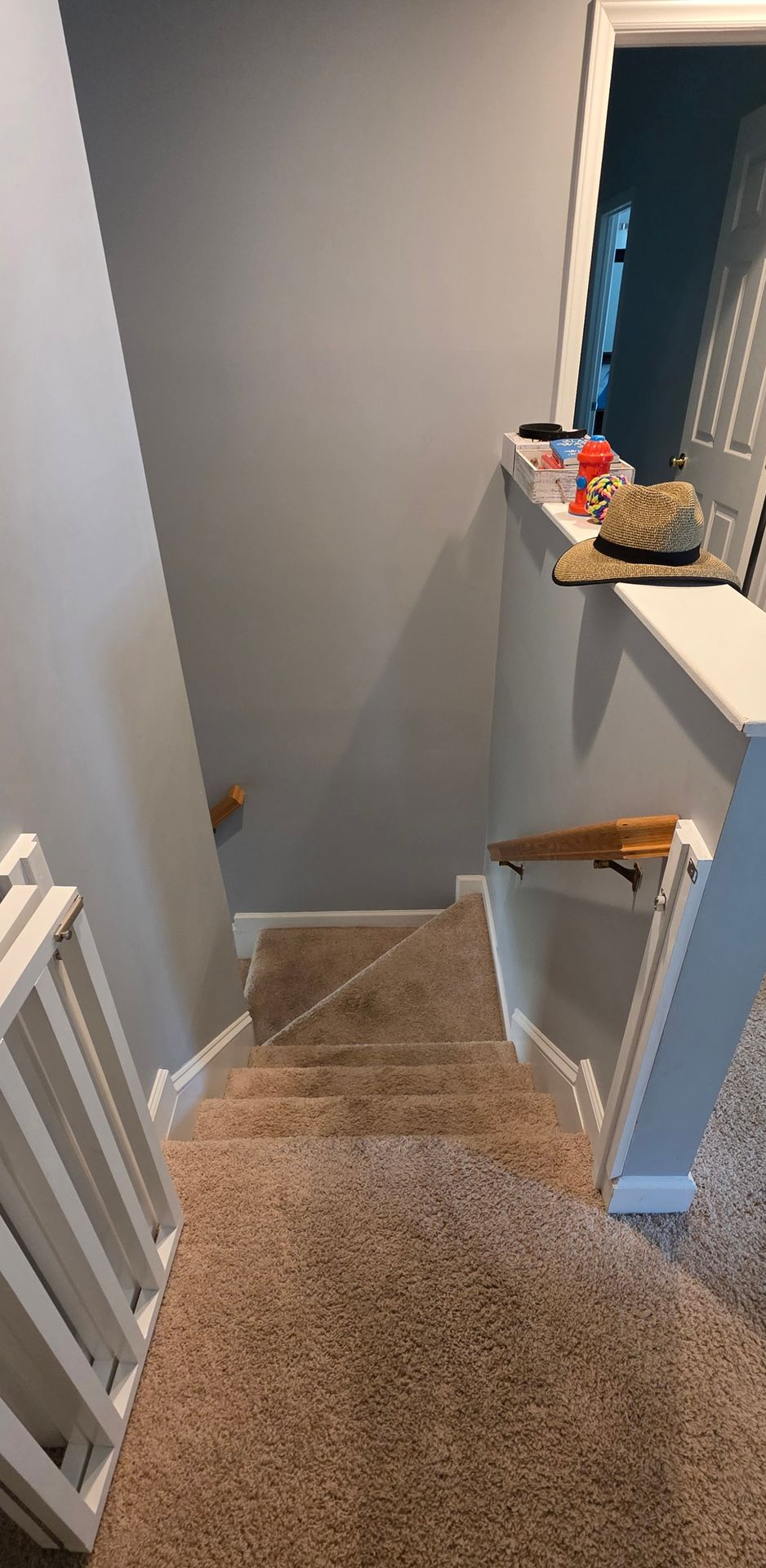 Carpeted staircase with white walls, wooden handrails, and a small shelf at the top landing.