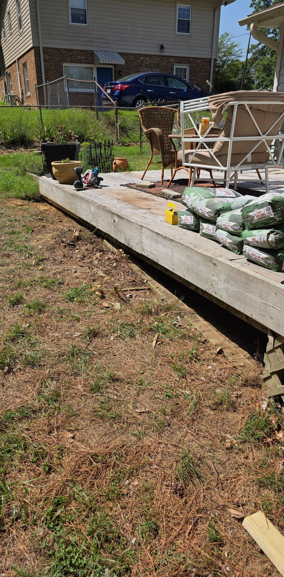 Backyard with a raised garden bed, potted plants, and stacked landscaping materials near a house.