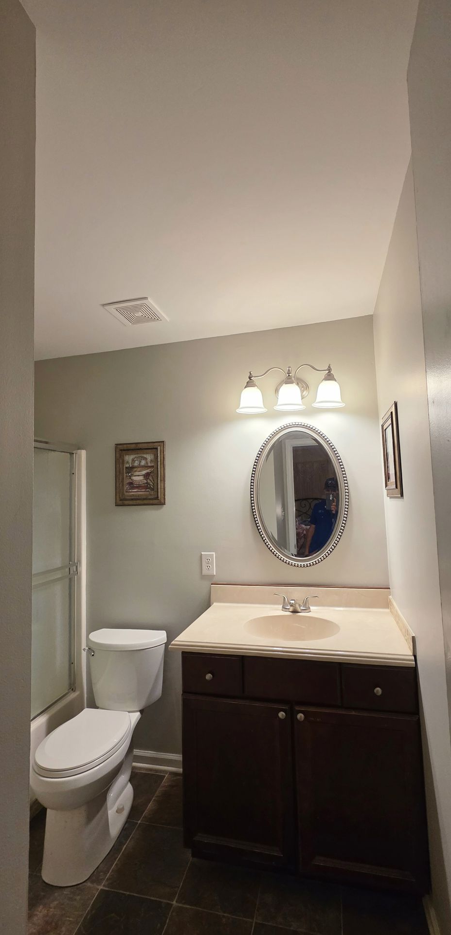 Small bathroom with toilet, vanity sink, oval mirror, and three light fixtures above.