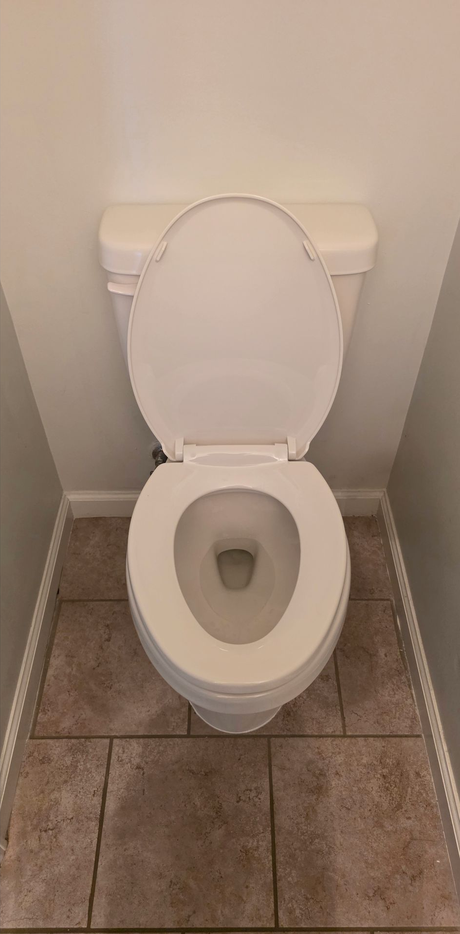 Open toilet with white seat in a small tiled bathroom