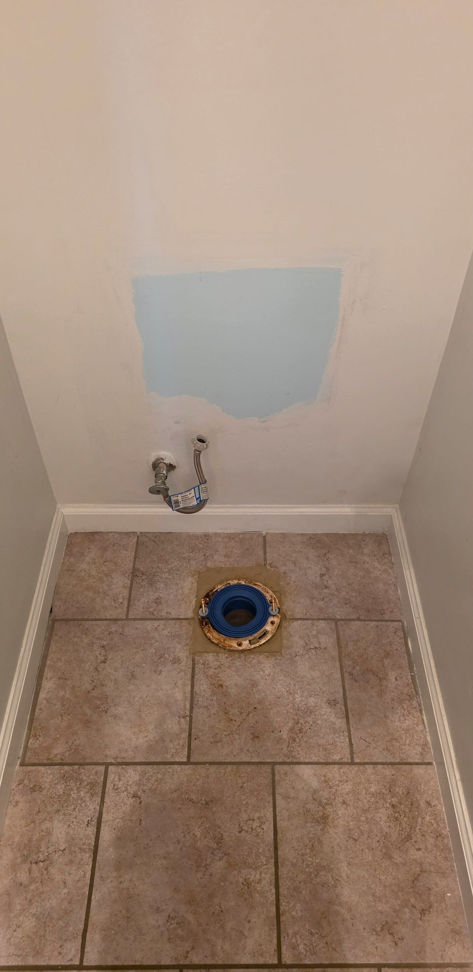 Small utility room wall with a blue patch, exposed pipe, and tiled floor with a floor drain.