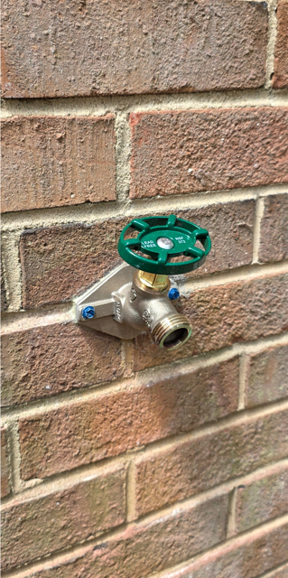 Green outdoor water shutoff valve mounted on a brick wall