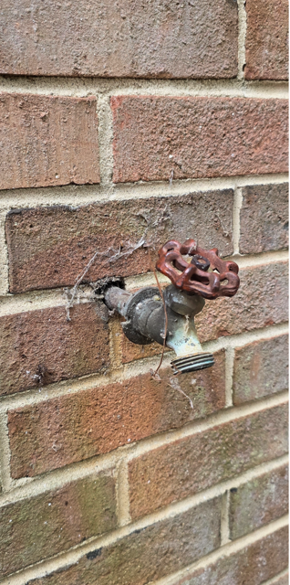 Water meter with red valve on a brick wall, with a small leak stain nearby