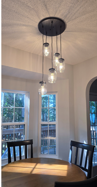 Dining nook with round table, black chairs, and modern pendant lights by large windows.