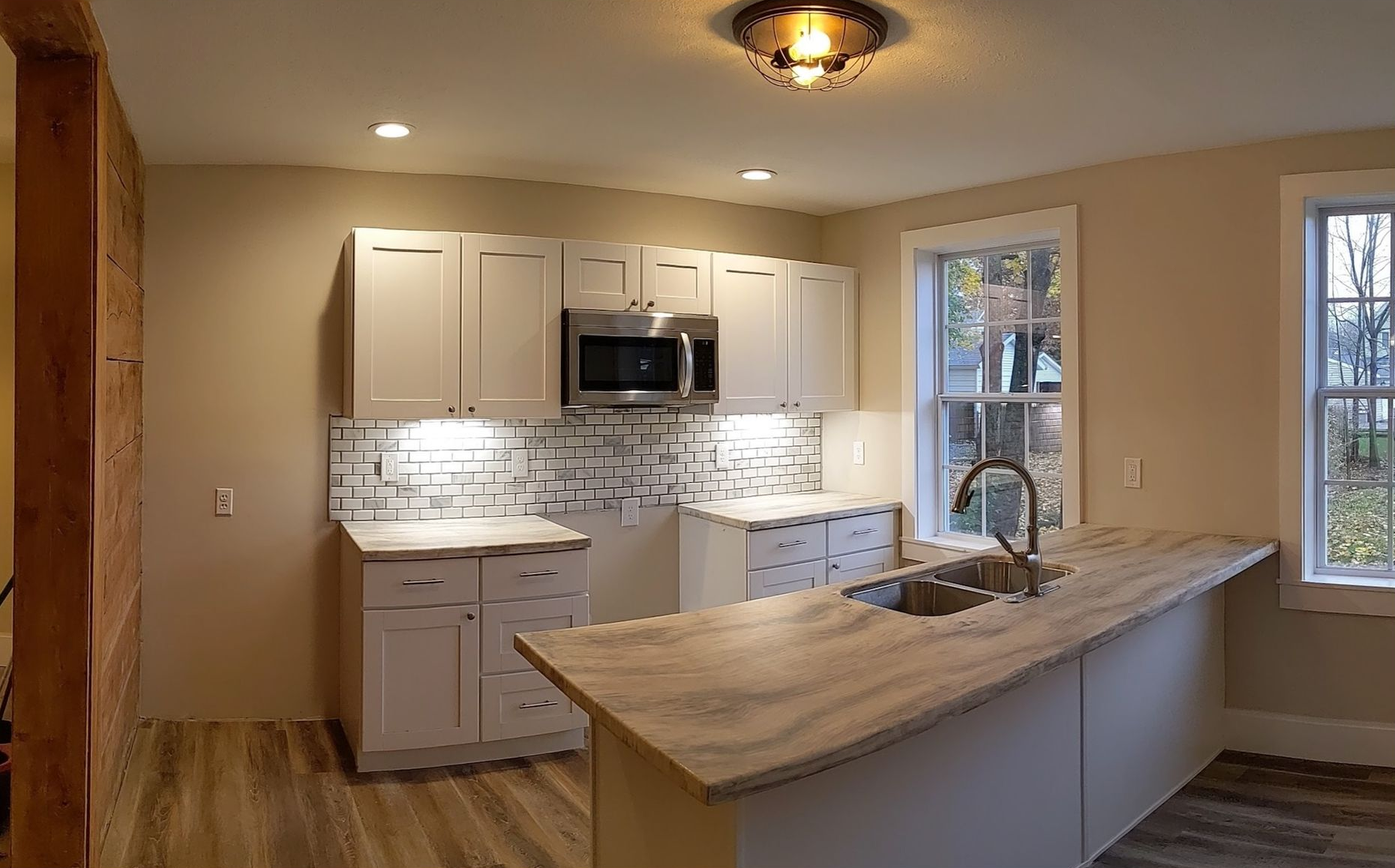 Bright modern kitchen with white cabinets, mosaic backsplash, and a large wooden island near windows.