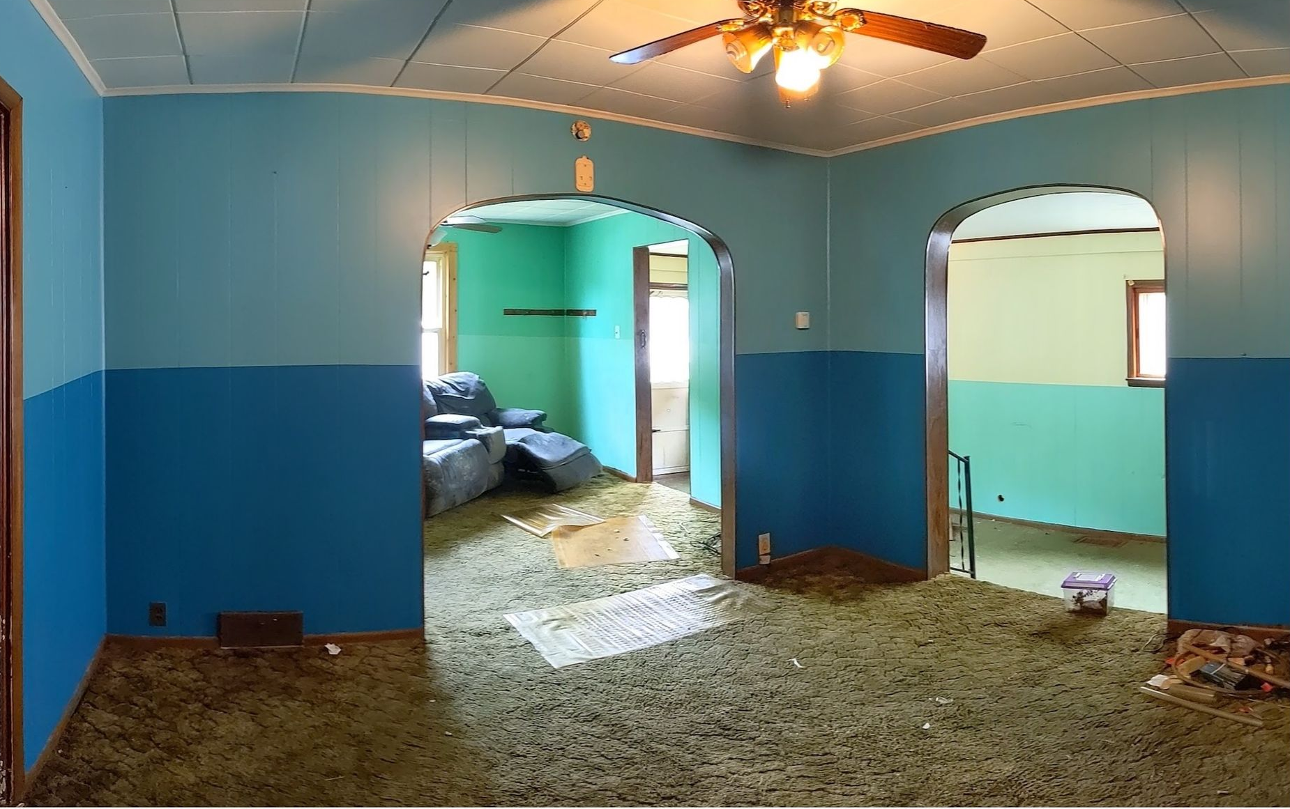 Empty blue room with arched doorways, exposed ceiling fan, and debris on the floor