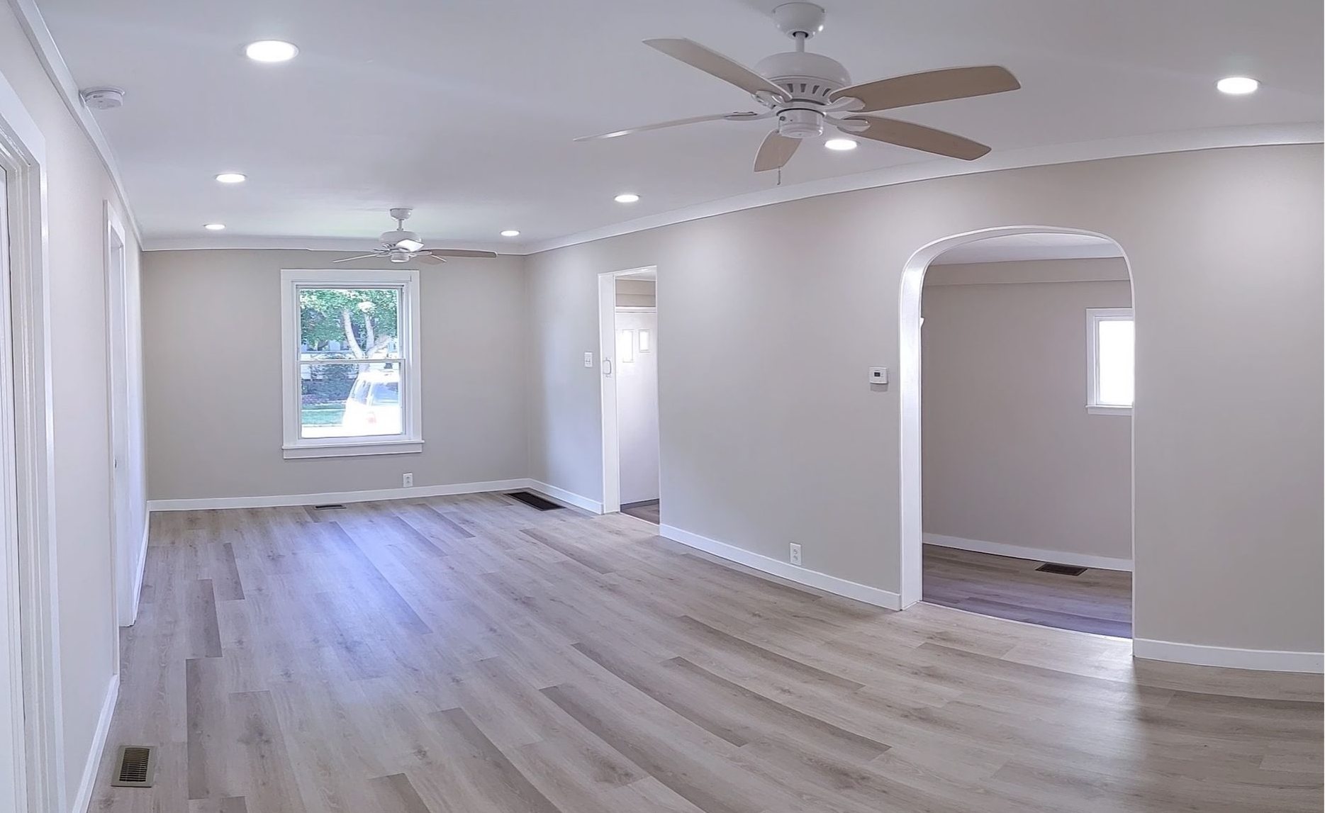 Bright empty living room with light wood floors, ceiling fan, and arched doorway to another room