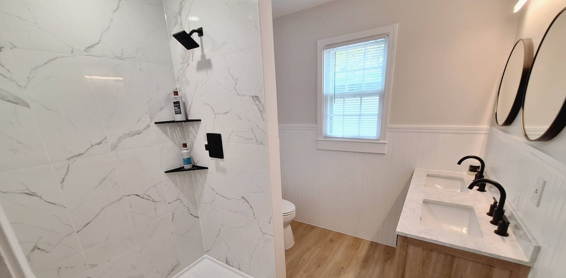 Bright white bathroom with marble shower, floating shelves, window, and wall-mounted sink.