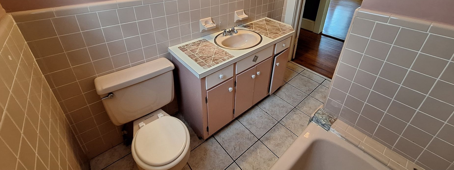 Small bathroom with toilet, double-sink vanity, and bathtub in beige tile.