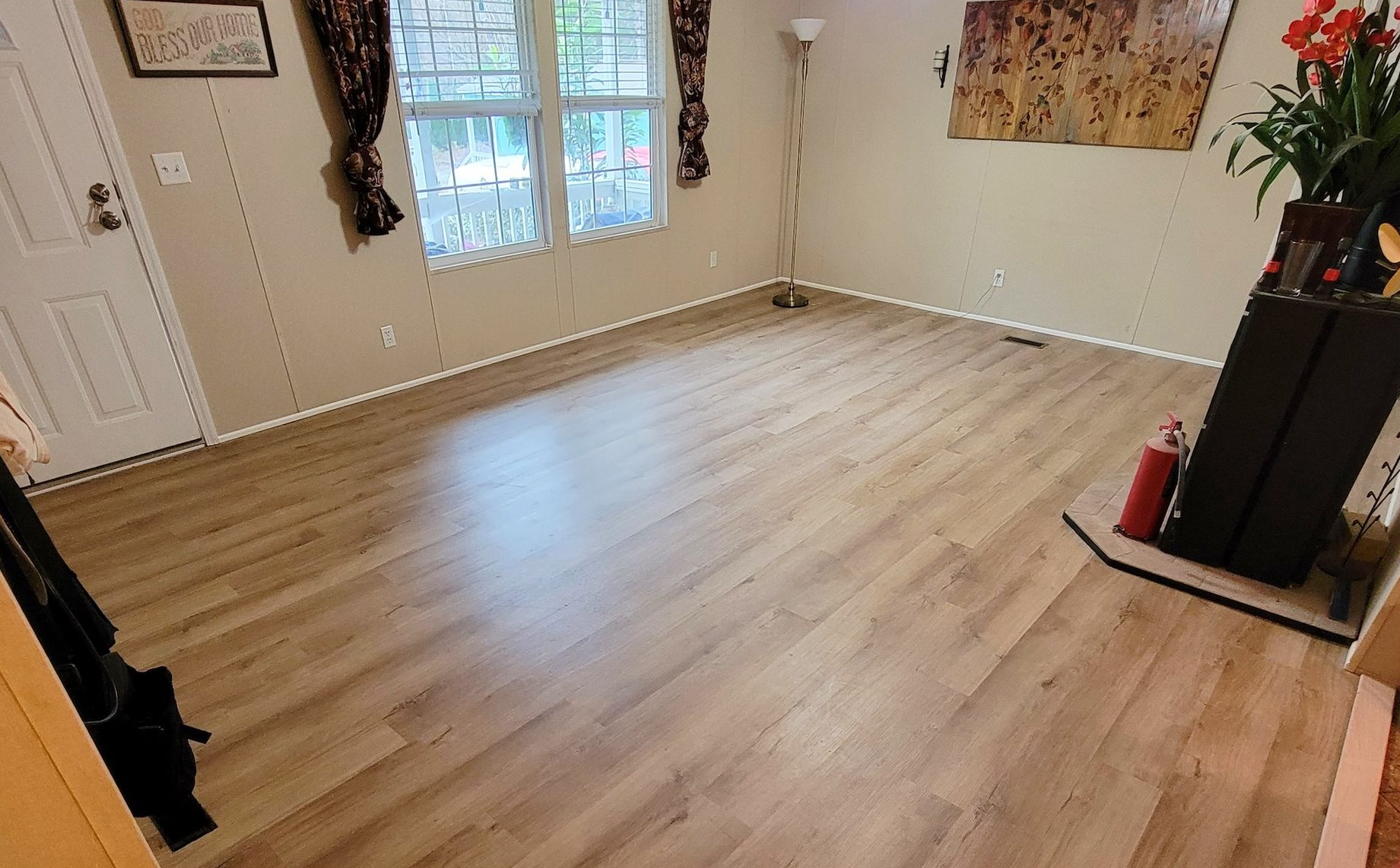 Empty living room with light wood flooring, white walls, and large windows letting in natural light.