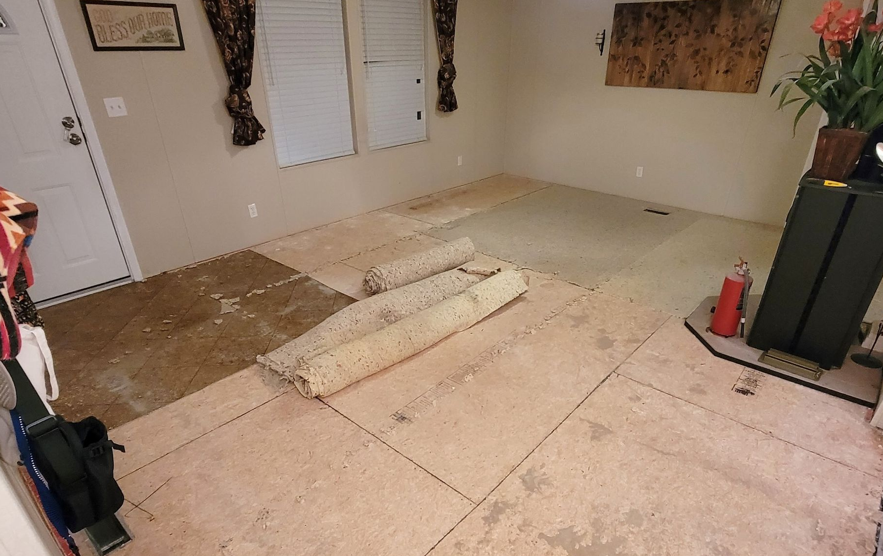 Partially stripped bedroom floor with plywood underlayment, tools, and paint cans during renovation