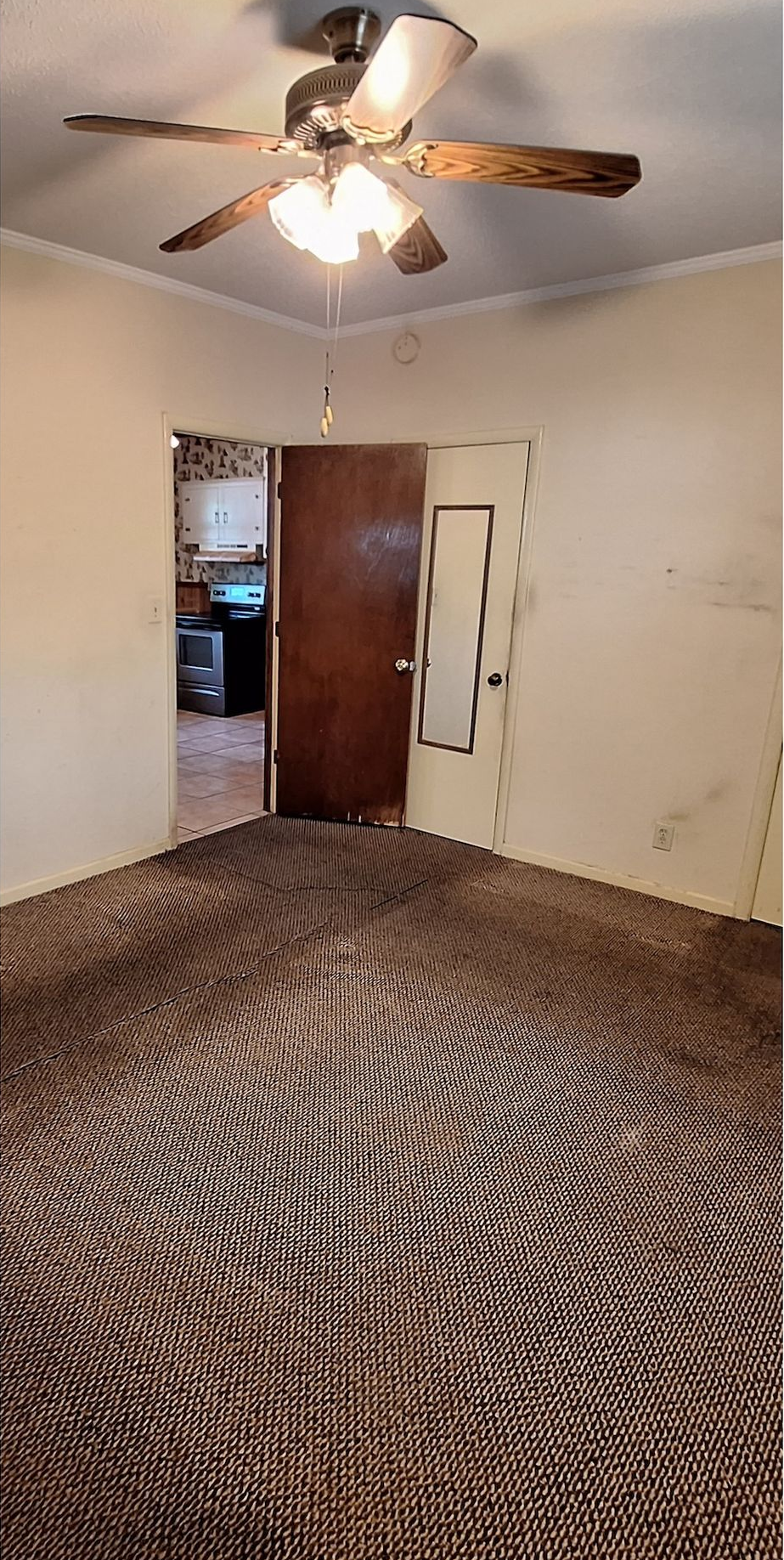 Empty carpeted bedroom with ceiling fan, doorway to another room, and partially open closet door