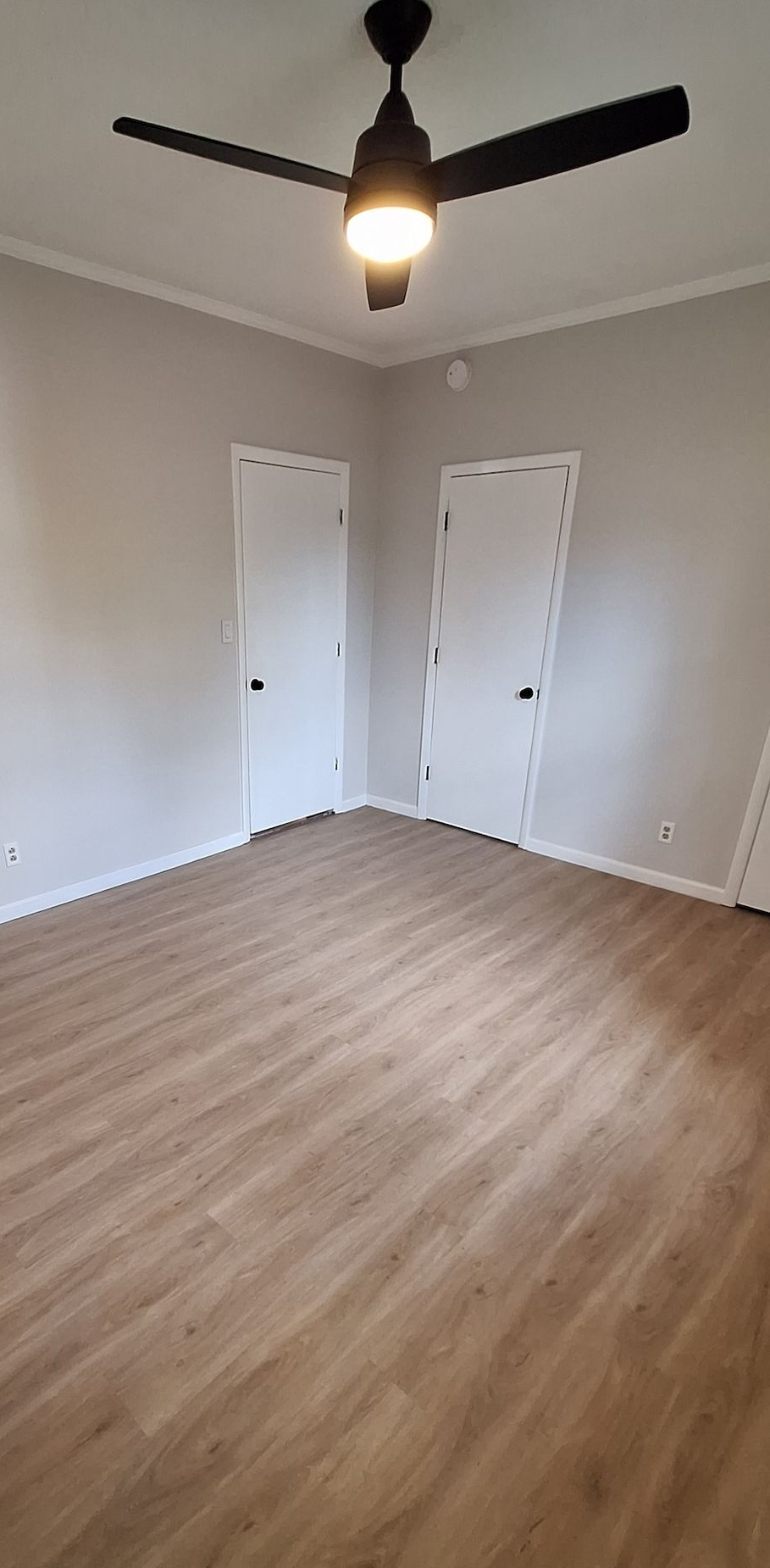 Empty beige bedroom with wood floors, white walls, two closet doors, and a ceiling fan with light.