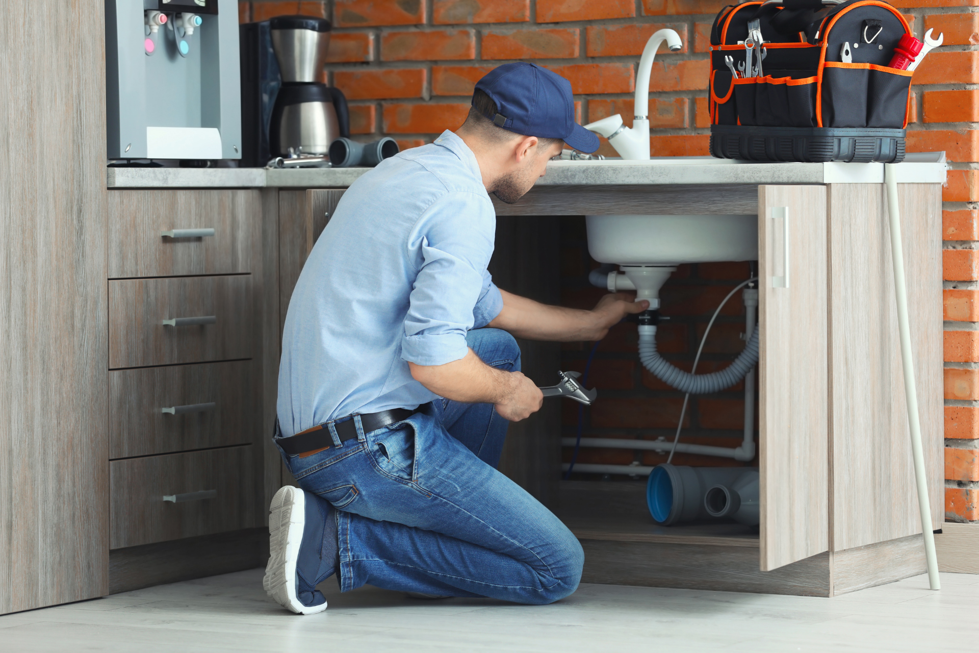 Plumber kneeling under a kitchen sink, inspecting pipes in a modern kitchen