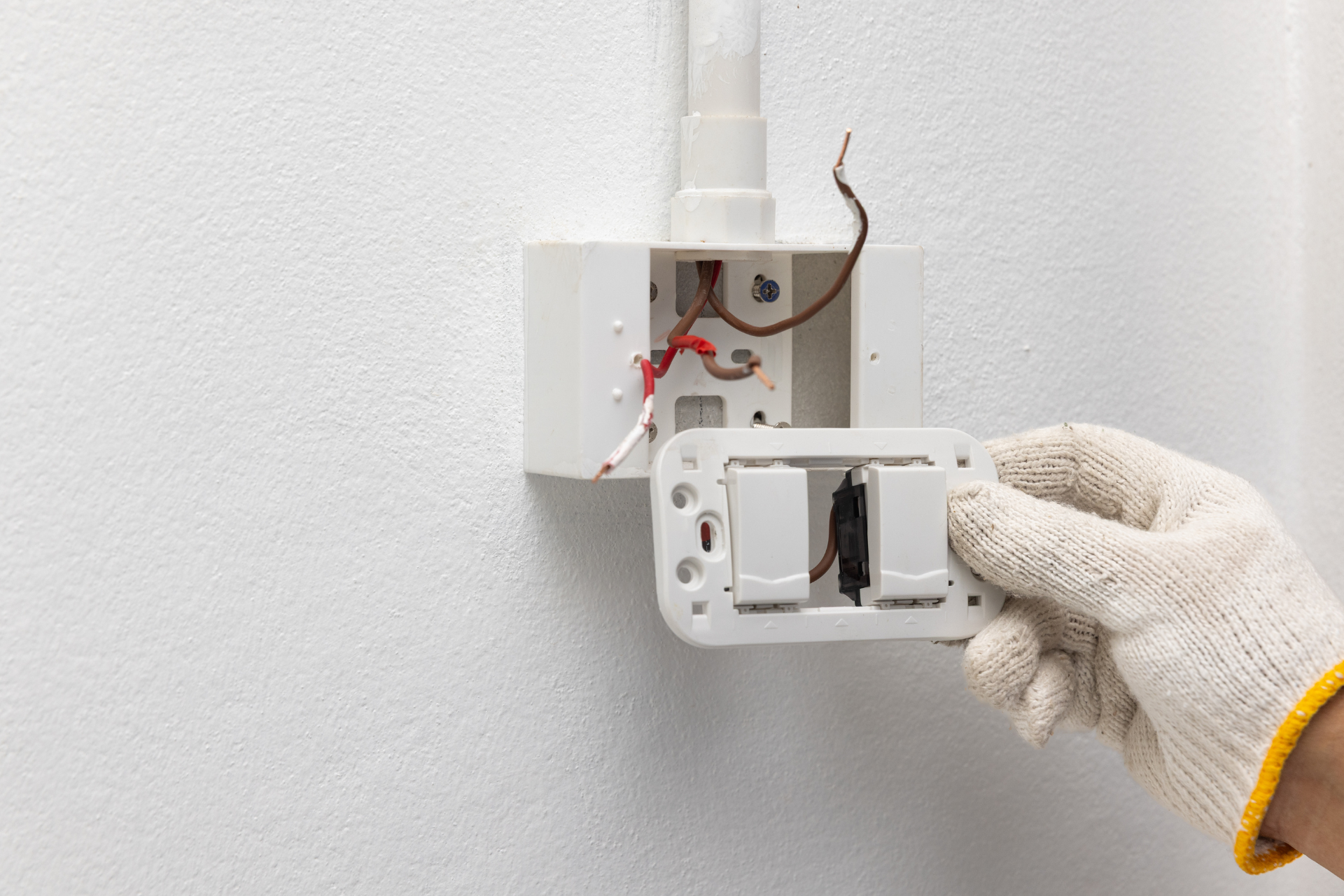 Gloved hand installing a wall light switch cover on a white electrical box