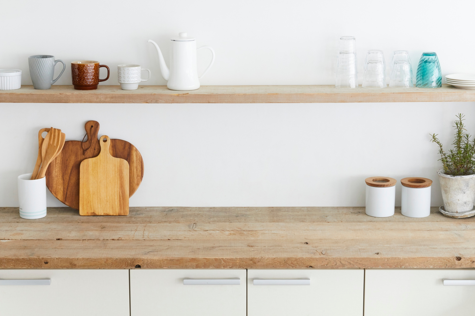 Minimal kitchen counter with wooden cutting boards, white dishes, and jars on open shelves