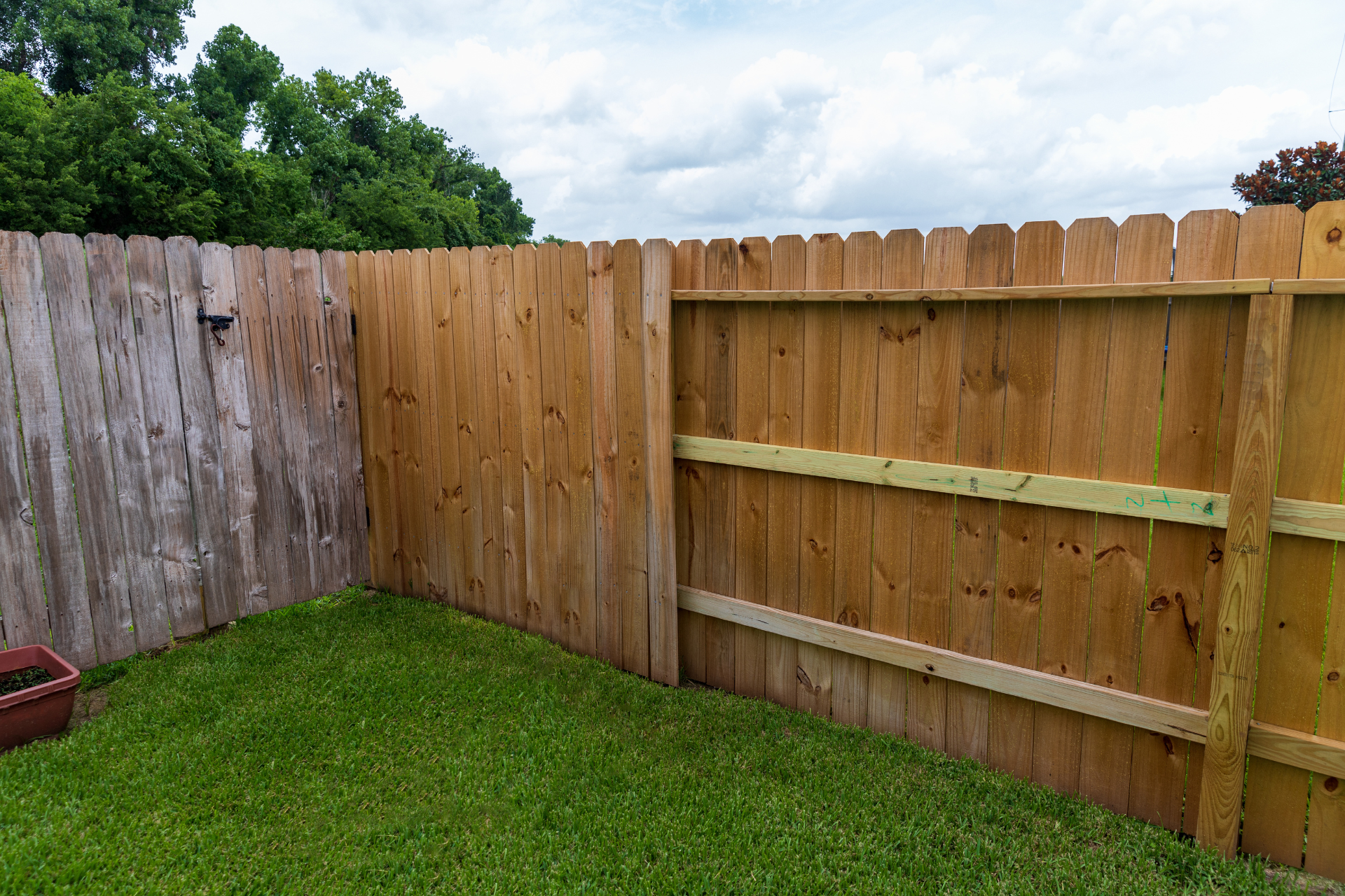 Wooden backyard fence with a grassy lawn and partly cloudy sky above