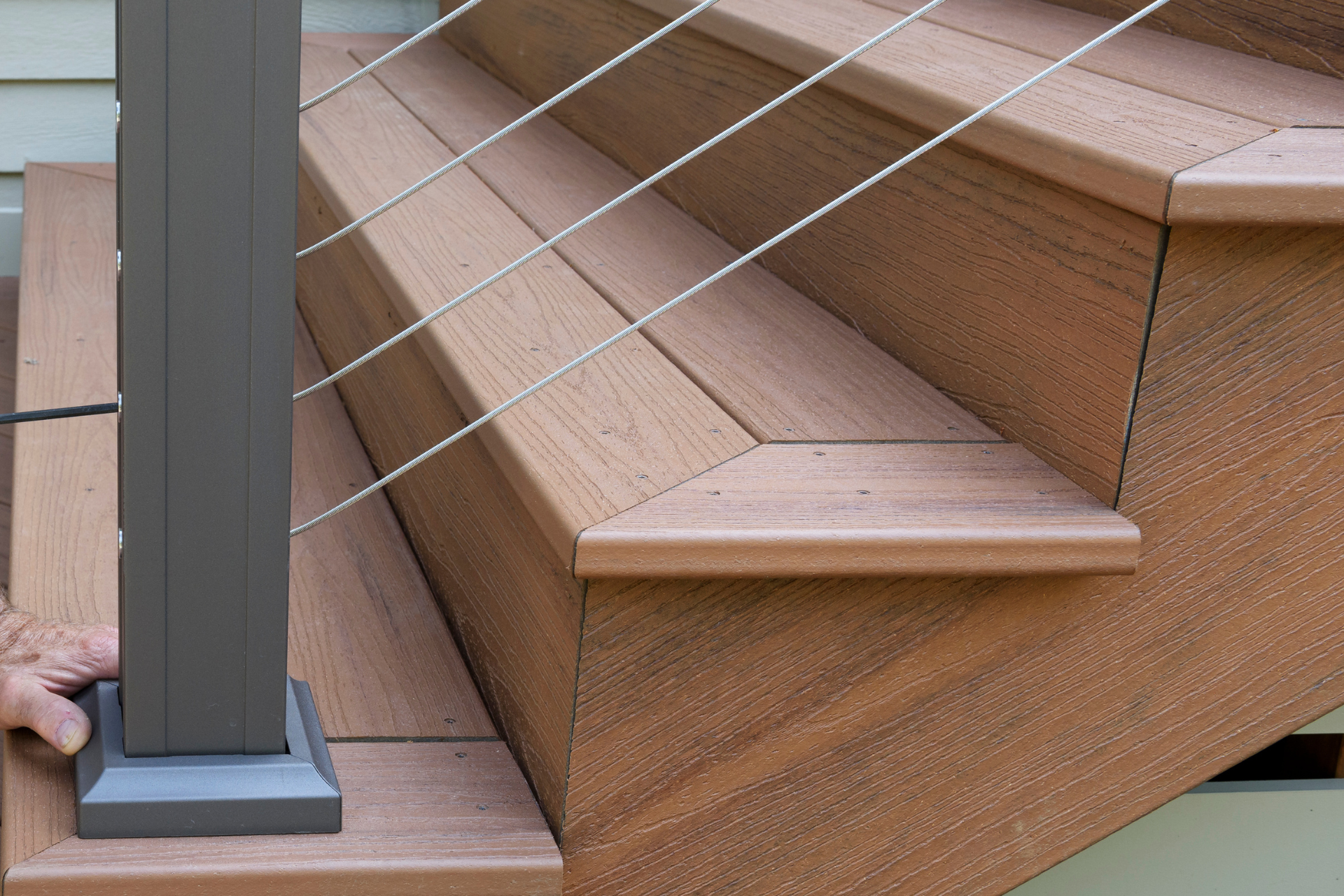 Outdoor wooden stairs beside a gray post, with diagonal support wires and beige trim