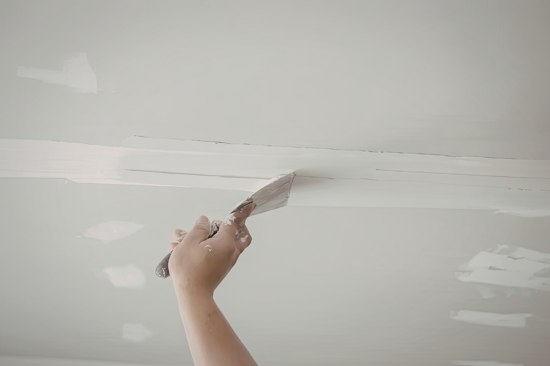 Hand spreading white compound on a ceiling seam with a putty knife