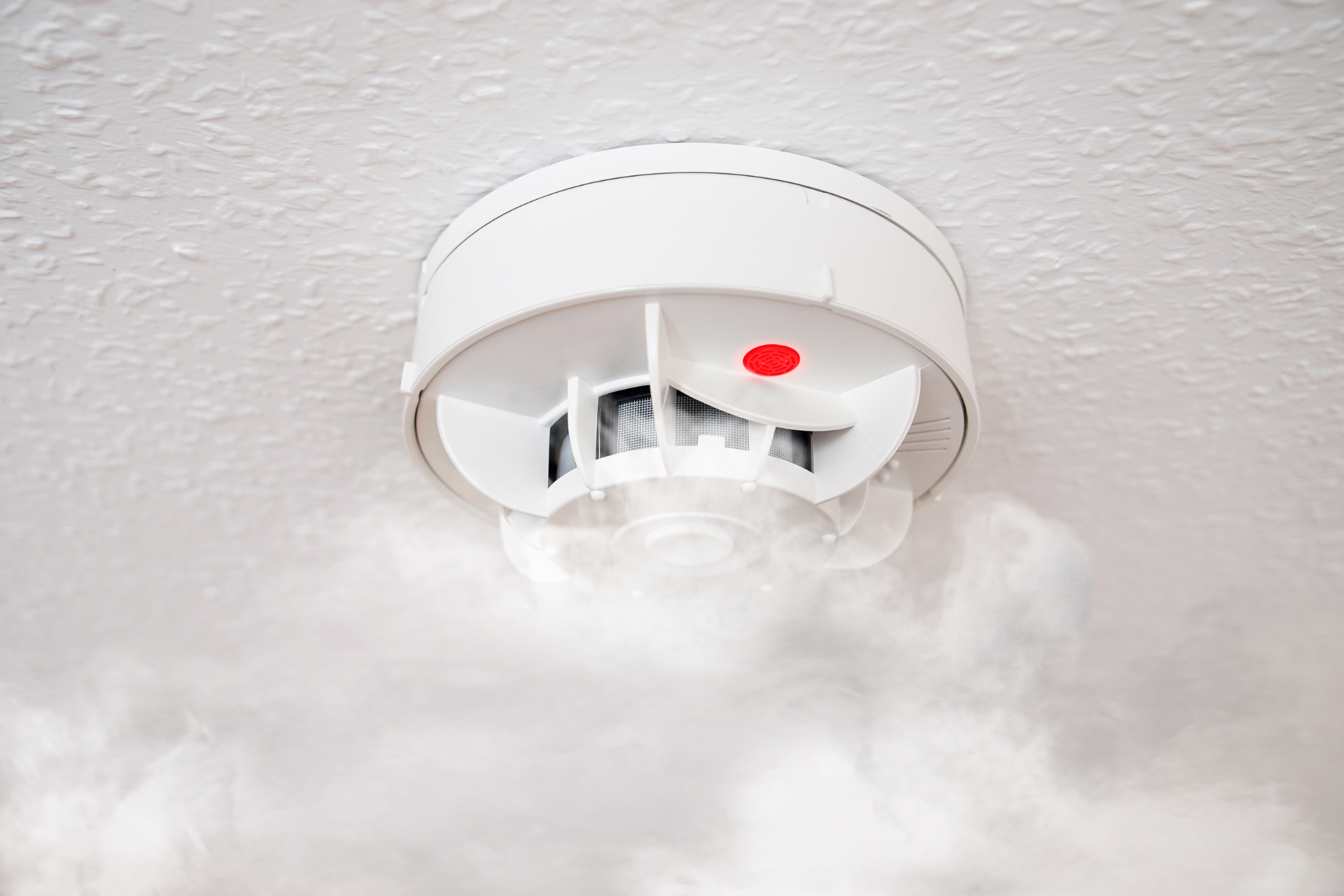Ceiling smoke alarm sounding, with thick smoke rising beneath it